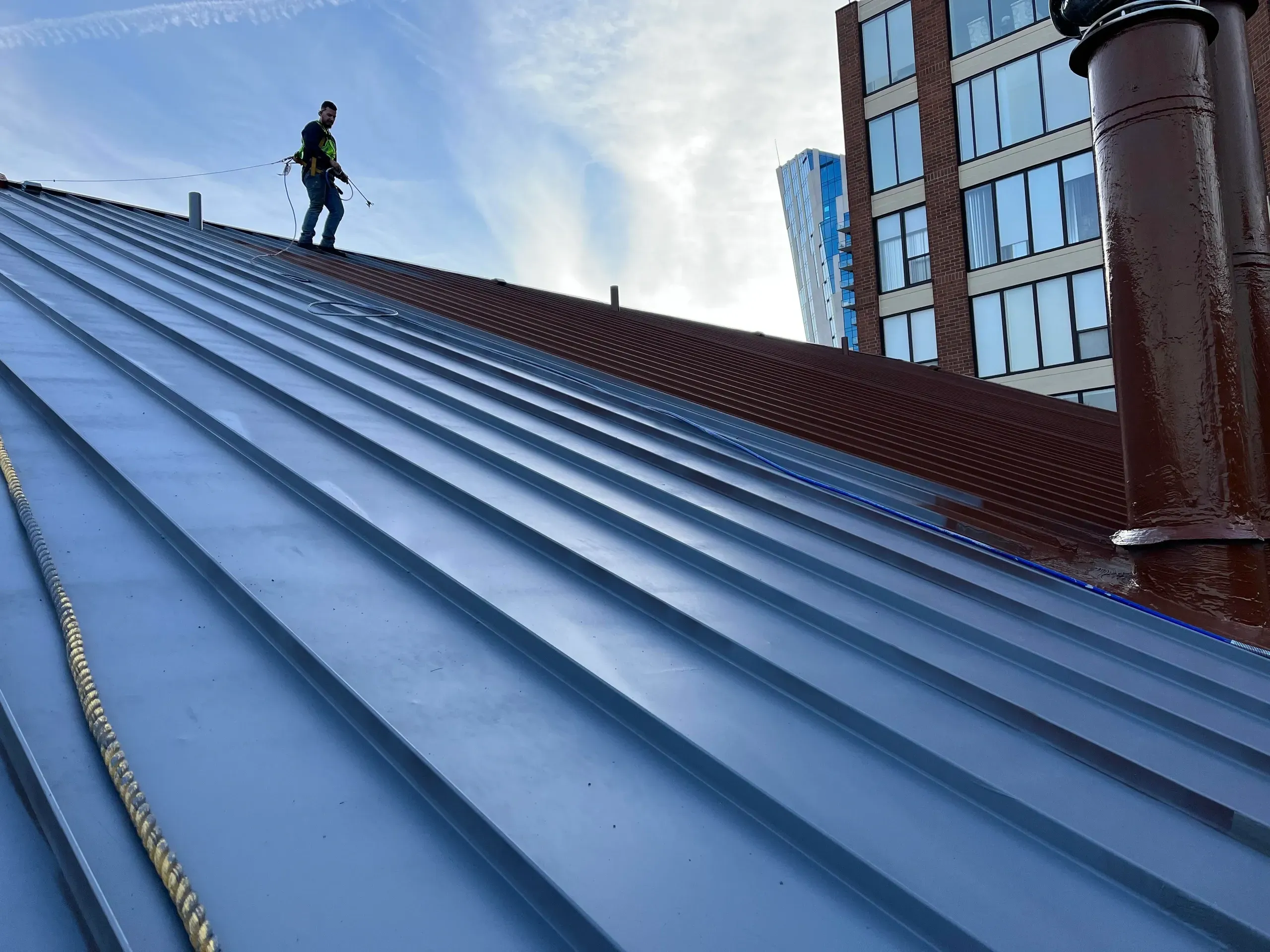 Worker applying coating on a sloped industrial metal roof